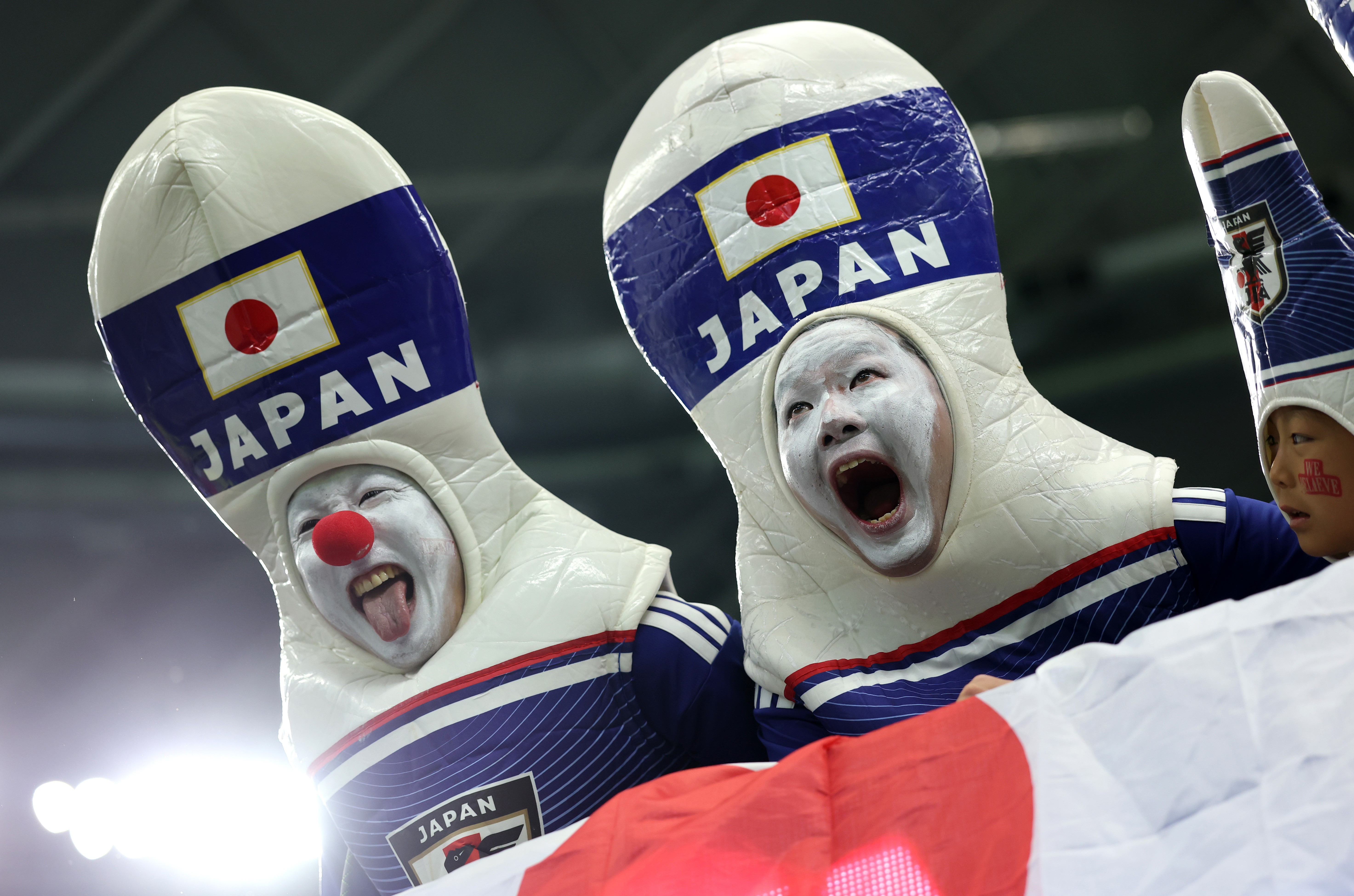 Fans of Team Japan, wearing bowling-pin costumes, cheer in a stadium.