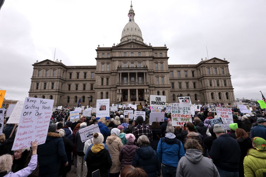 Sign-carrying protesters stand outside a state capitol building.