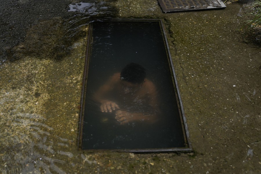 A boy submerges himself to cool down in a flooded hole in a street.