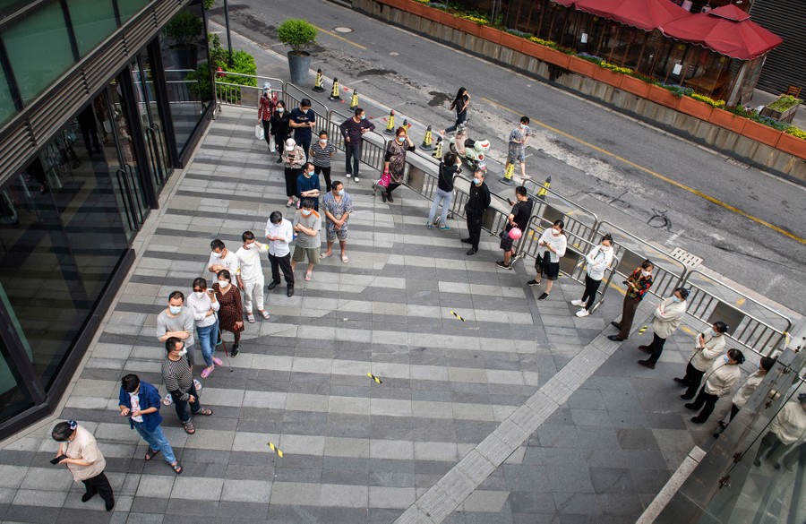 About 25 people can be seen standing in a line along a city street.