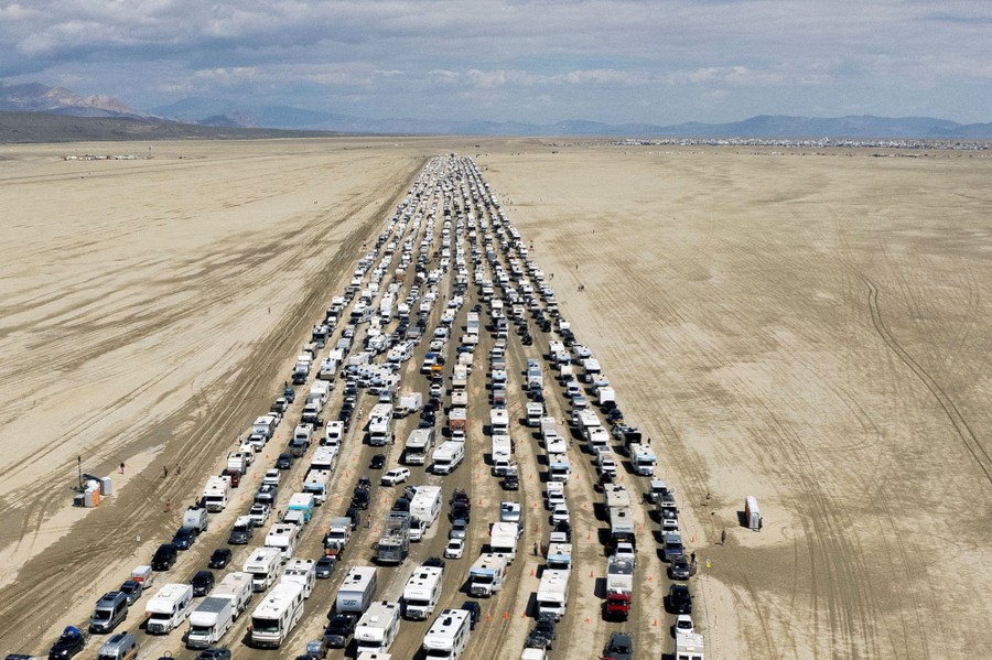 An aerial view of at least ten lanes of hundreds of cars and RVs lined up in a desert