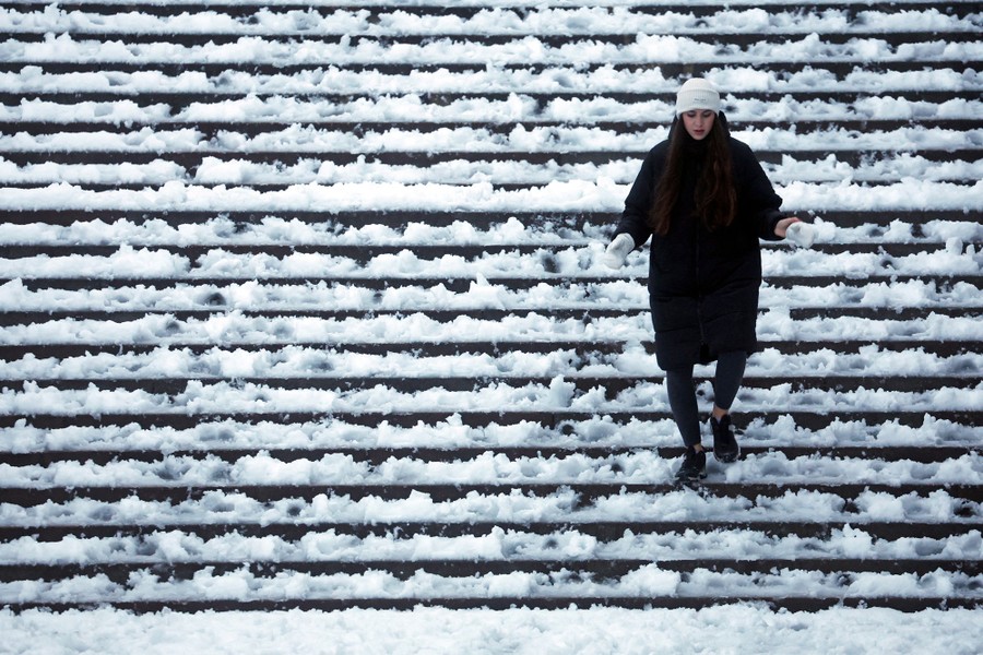A woman walks down a wide snow-covered set of stairs.
