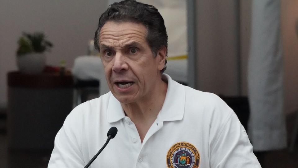 Andrew Cuomo in a white shirt in front of a microphone
