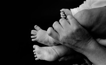 an adult's hand holds up a baby's feet, in greyscale