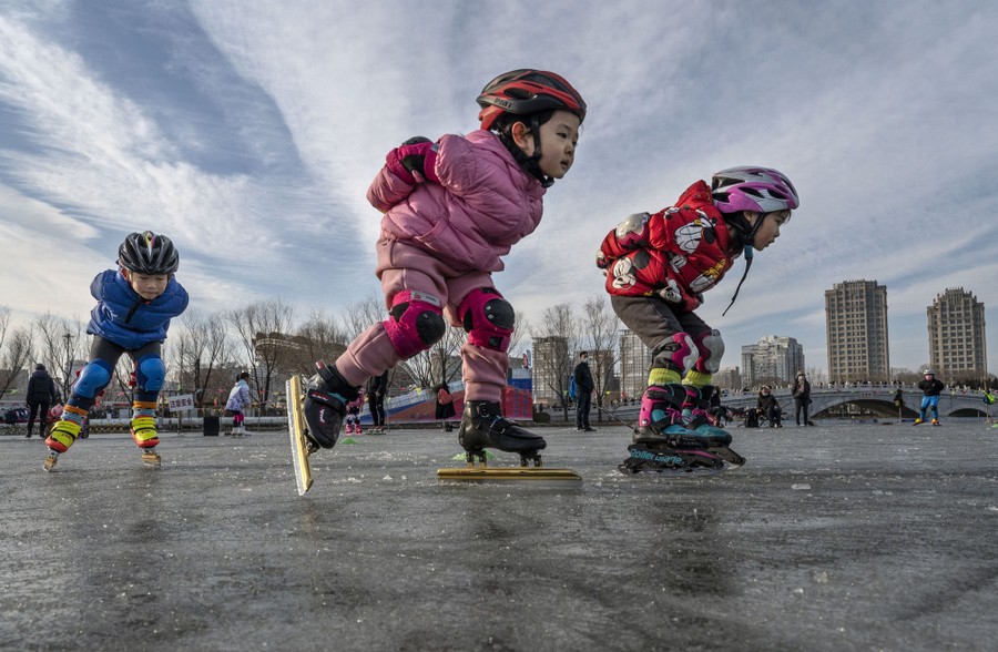 Several children take part in speed-skating lessons at an outdoor rink.