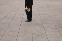 A person dressed in all black stands holding a microphone in the middle of an empty plaza