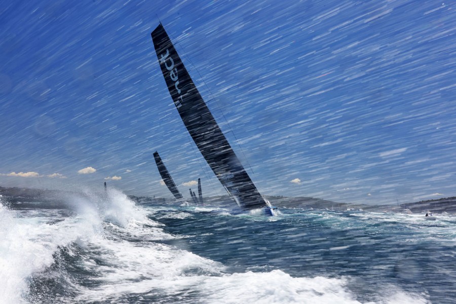 Several yachts lean with the wind, sailing in a harbor.