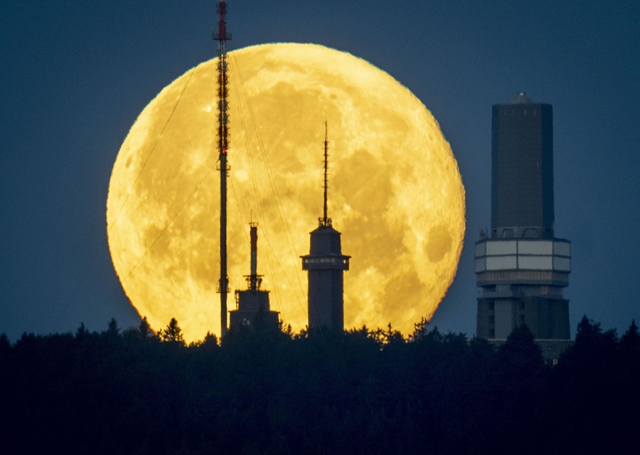 The full moon sets behind telecommunication towers.