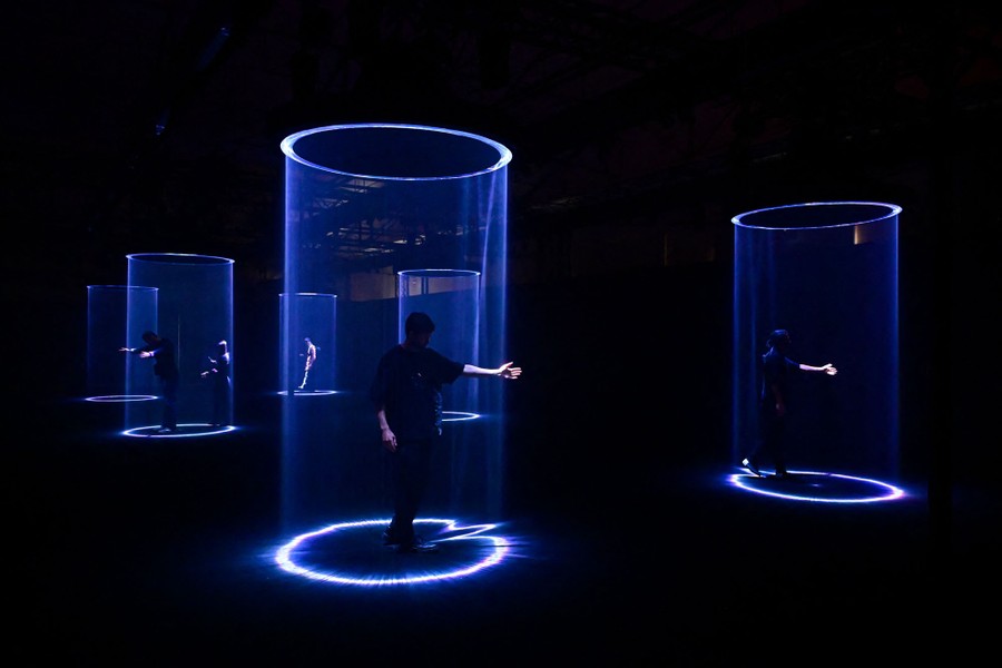 People play with an art installation, which consists of rings of bright light shining from a ceiling in a dark room, forming tubes of light.
