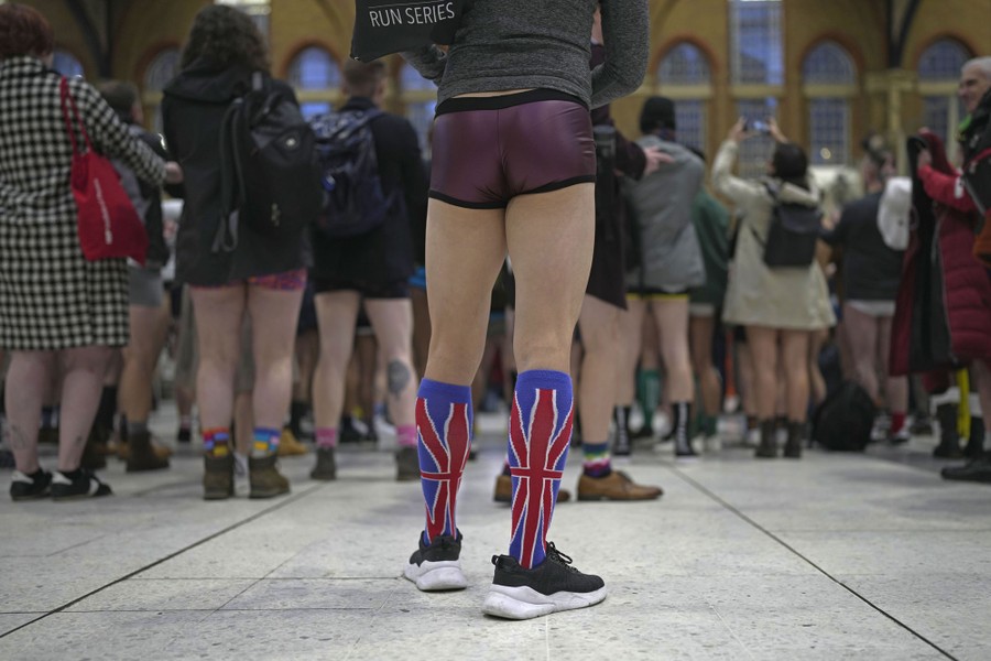 A group of people wearing regular street clothes—except pants—stand in a train station.