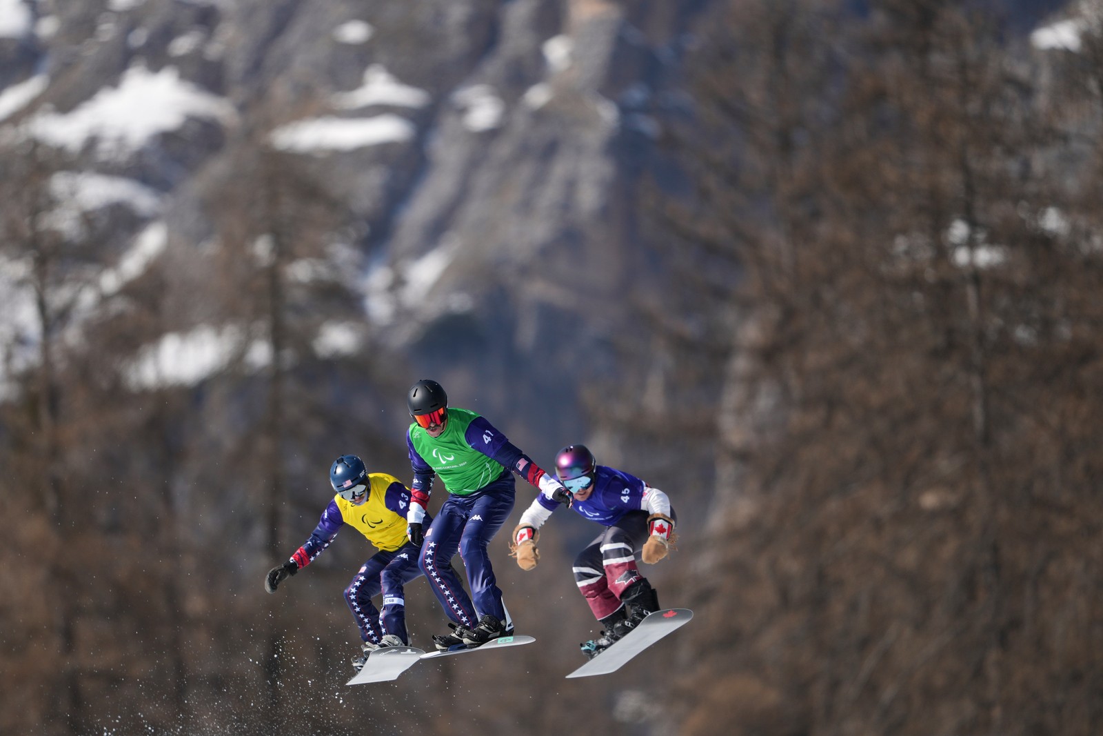 Three snowboarders catch some air during a Paralympic event race.