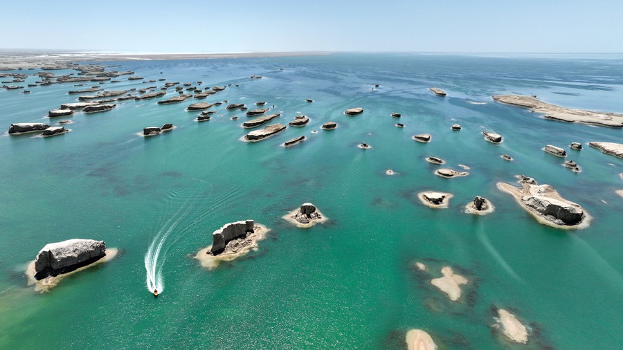 A small boat weaves between multiple rock formations that make up dozens of tiny islands in a turquoise lake.