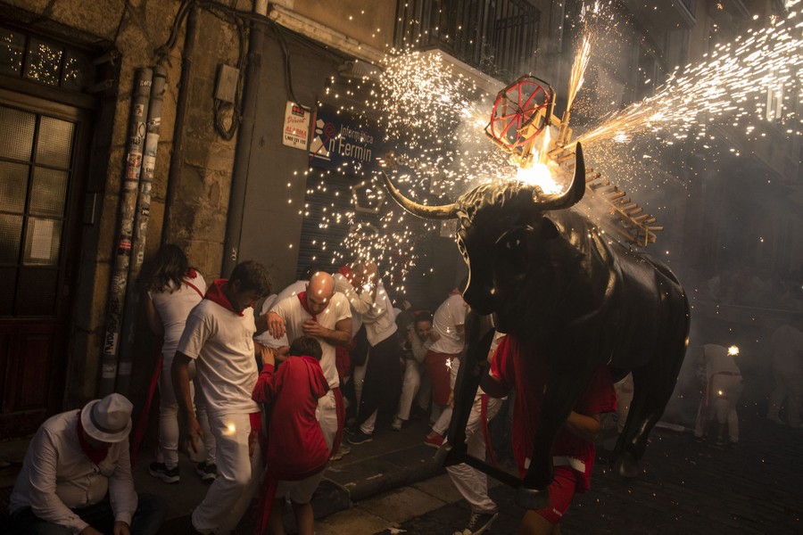 People in a street cower and run from a statue of a bull with sparking fireworks erupting from its back.