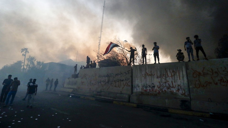 Iraqi protesters wave a national flag while standing on barricades outside the burned-down headquarters of the local government in Basra on September 7.