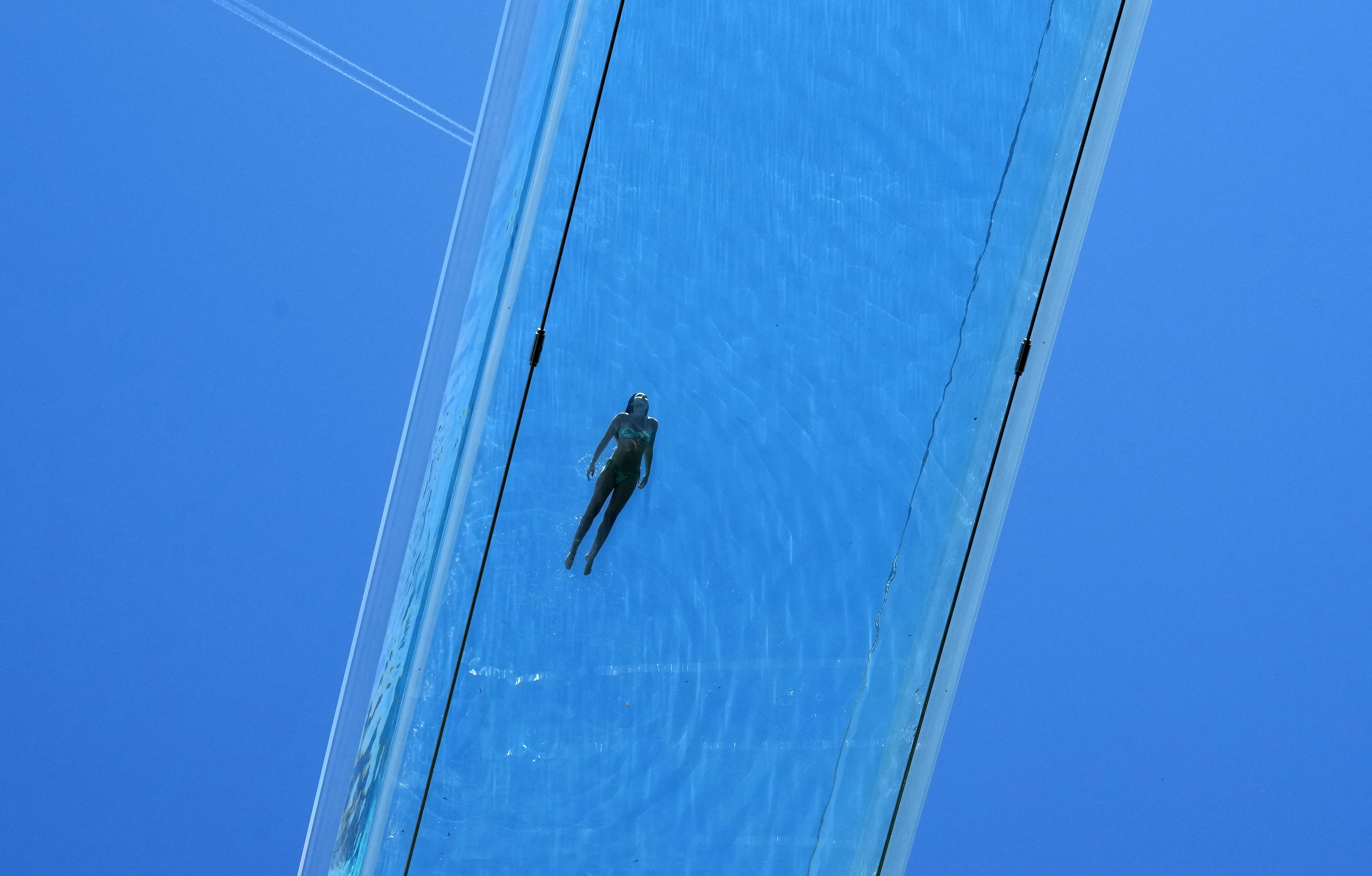 A person swims in a transparent acrylic swimming pool bridge, seen from below.