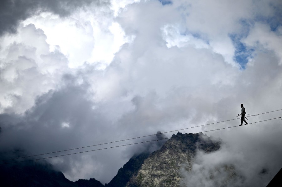 A tightrope walker is seen among mountains and clouds.