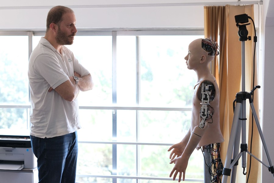 A man stands facing the upper half of a humanoid robot.