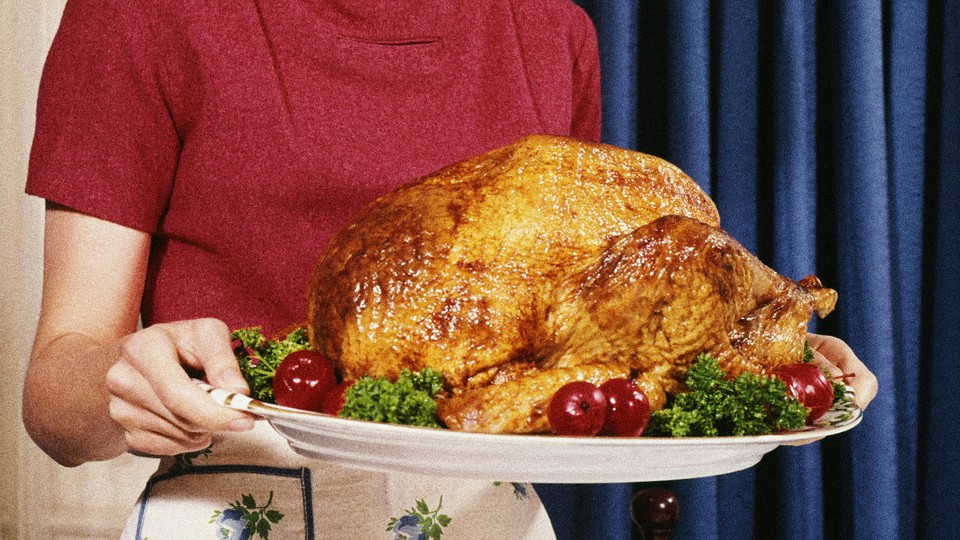 A person in a pink shirt and white skirt holding a tray with a roasted turkey on it