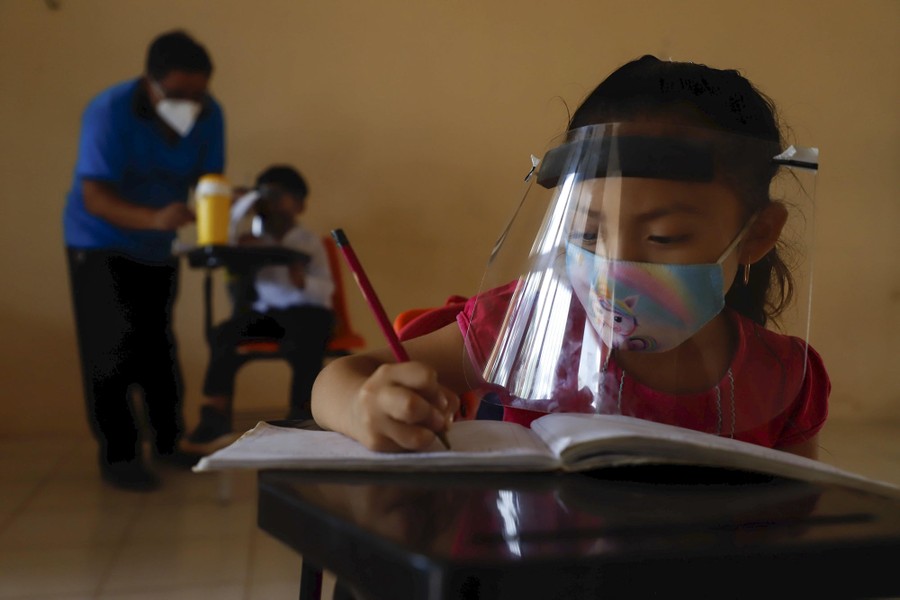 Young students sit in desks spaced far apart inside a classroom.