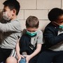 A group of young kids in face masks sit on a bench.