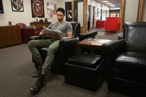 A man sits in a leather chair reading a textbook.