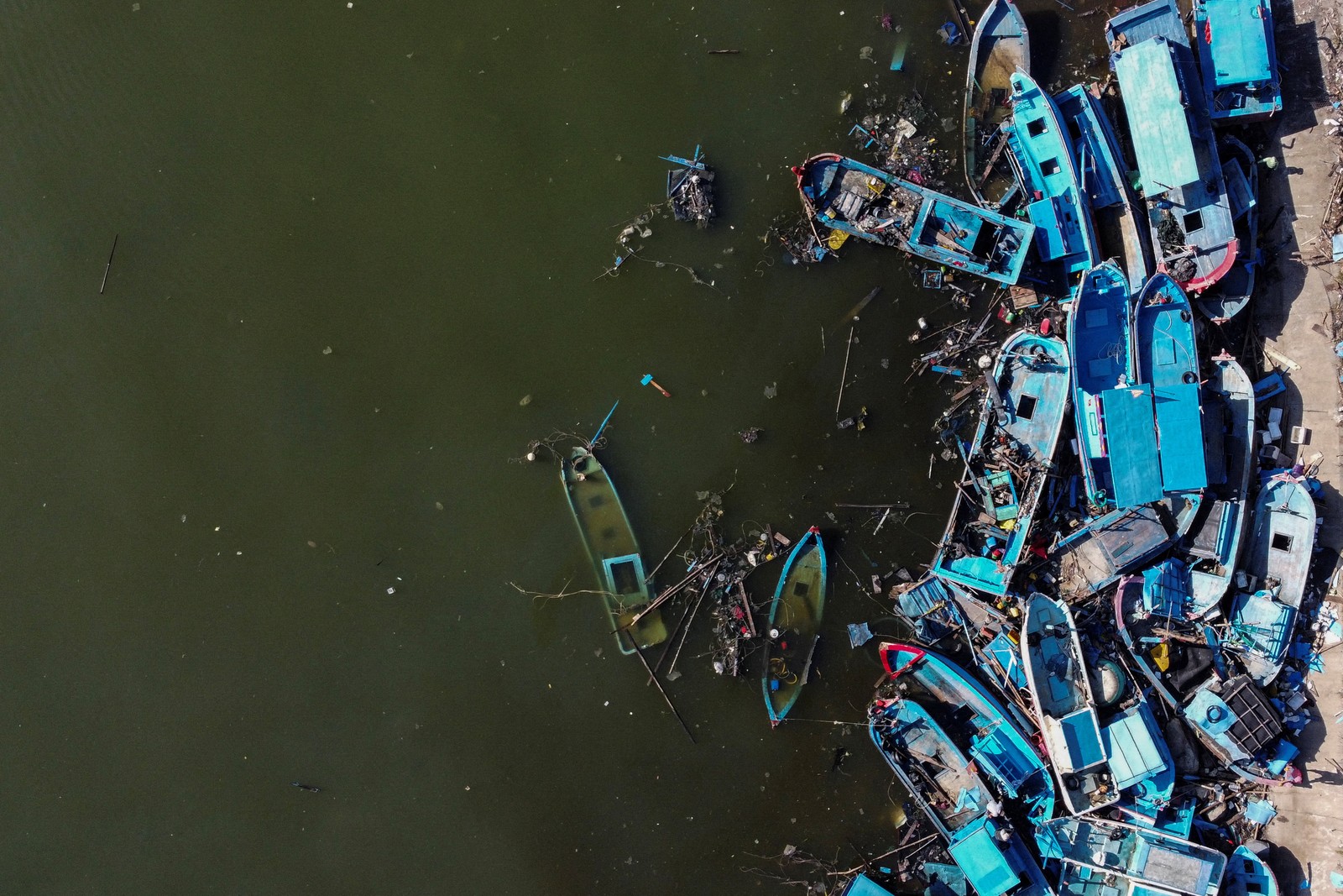 A drone view of small fishing vessels piled up in wrecks along a shoreline after a typhoon passed through.