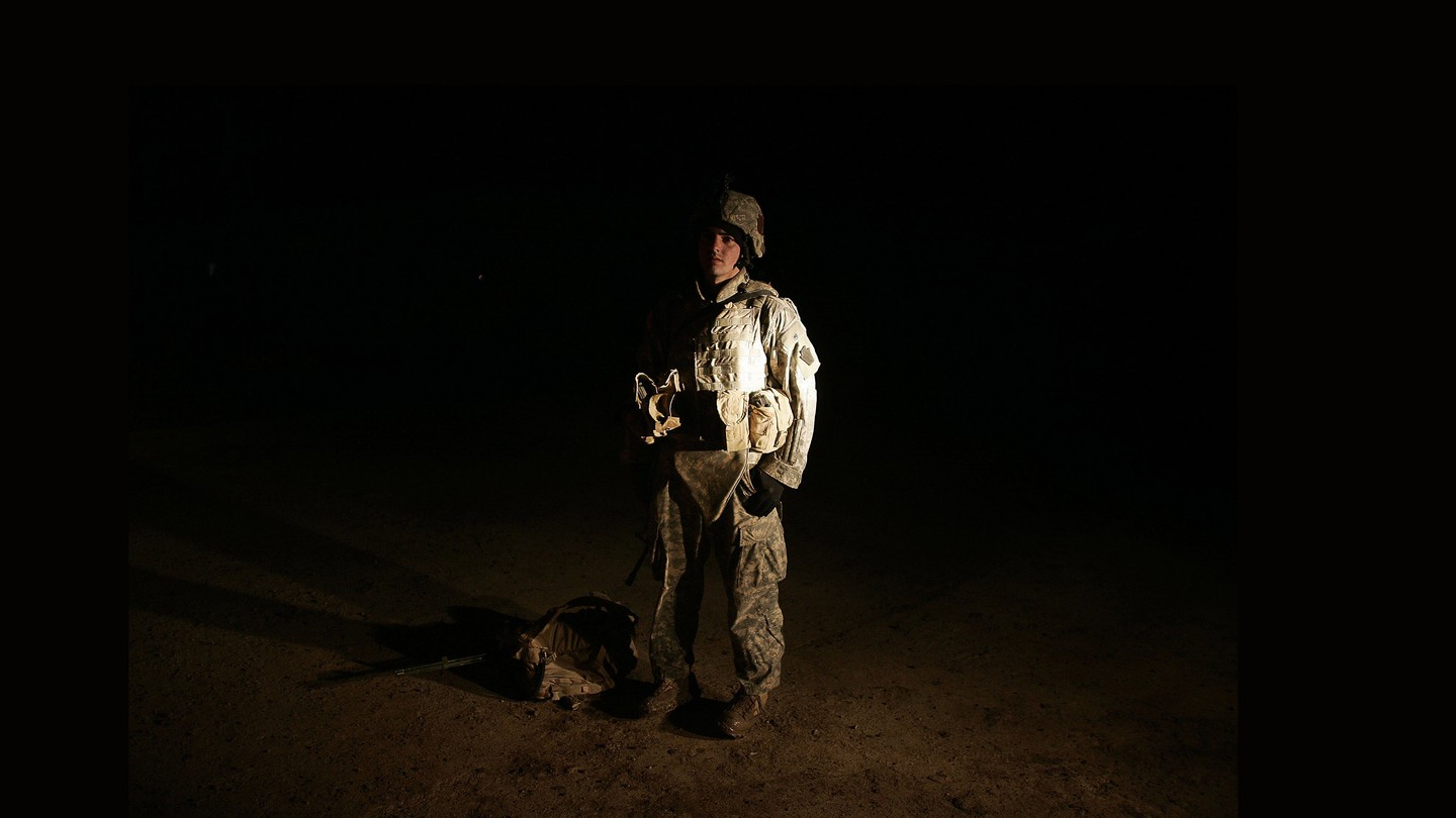 A photo of a man wearing camouflage, illuminated against a dark background