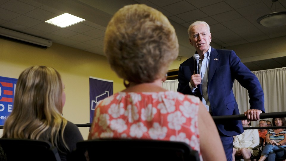 Joe Biden, wearing a blue suit and holding a microphone, speaks to a small crowd
