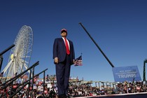 Donald Trump stands on stage at a rally with a giant ferris wheel and crane behind him