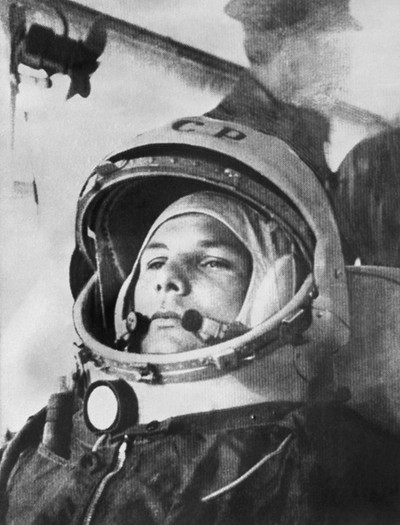 black-and-white photo of cosmonaut in full gear with large helmet and radio, sitting in vehicle