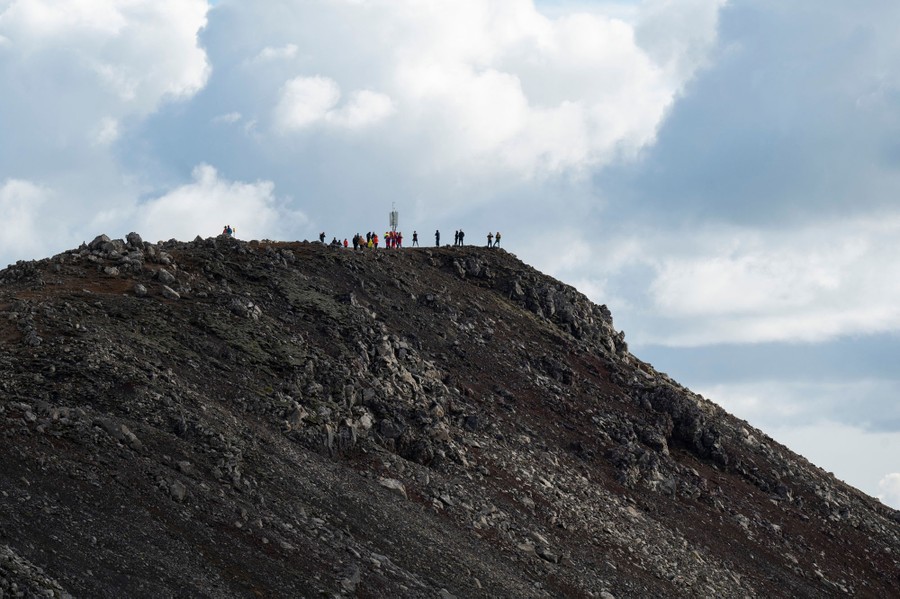 People stand on a rocky hilltop, looking toward an eruption (offscreen).