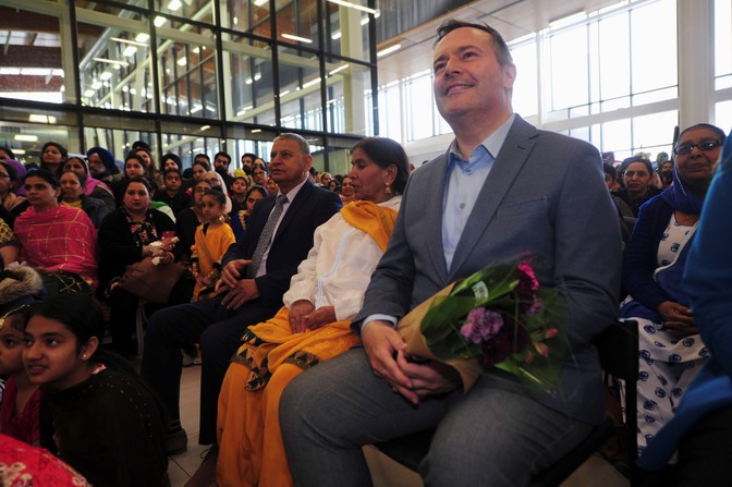 Jason Kenney sits at a Sikh community center holding a bouquet.