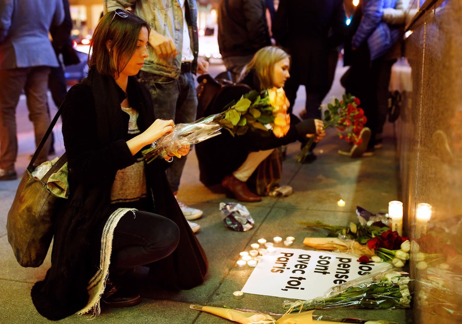 People place flowers and candles at a memorial.