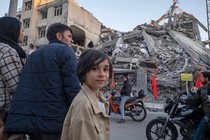 People including two young girls standing in front of rubble in a residential area in Tehran