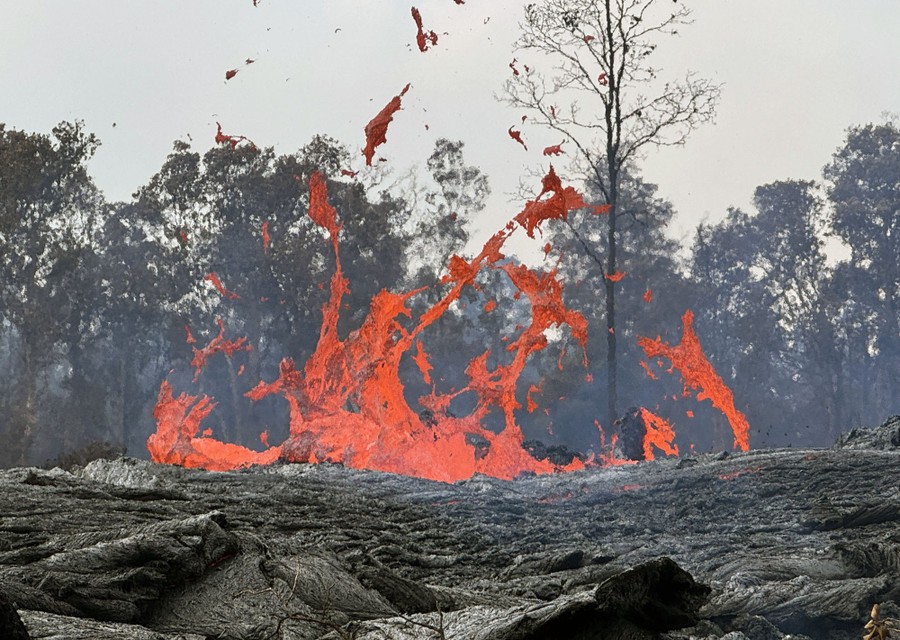 A distant view of splashing lava, backdropped by trees