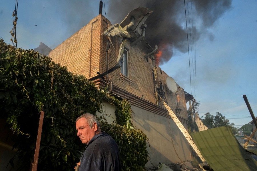 A person stands outside a burning house.