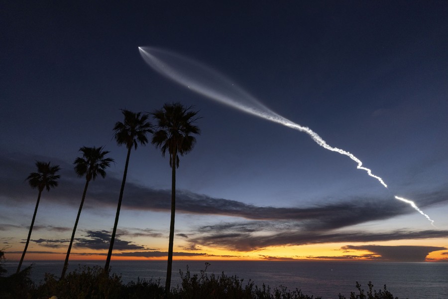 A rocket launch leaves a bright vapor trail across the night sky.