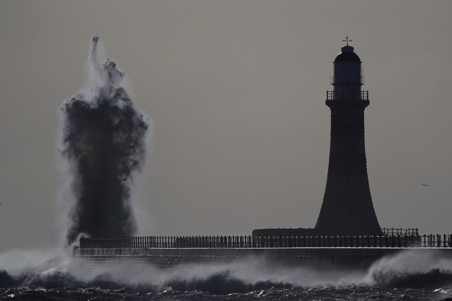 A huge wave splashes near a lighthouse.