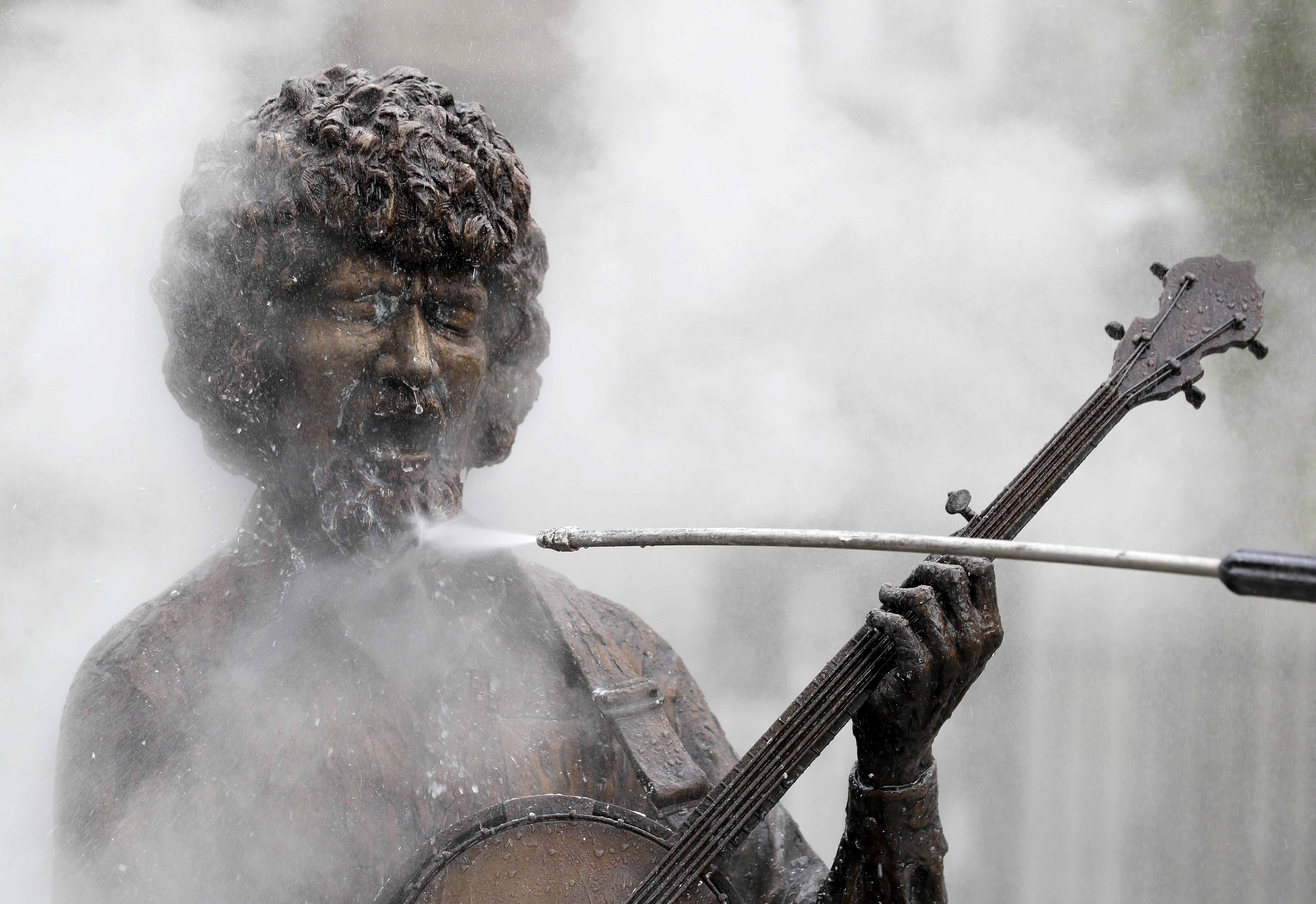 Water is sprayed from a wand onto the beard of a statue of a musician.