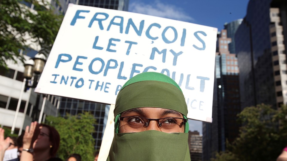 A woman in a niqab holds a placard at a protest.