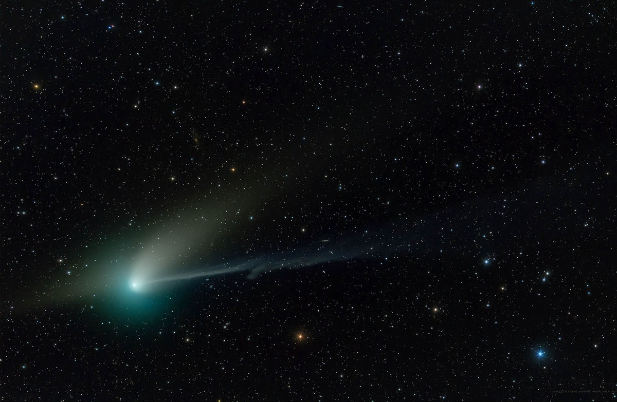 A comet, seen against a backdrop of stars. The comet looks like a bright, greenish smudge with two different 'tails'.
