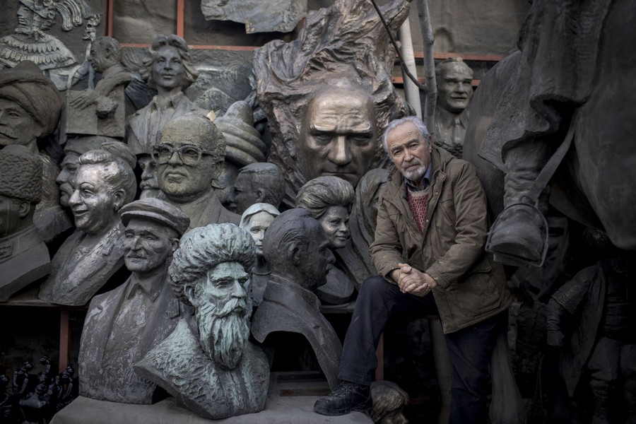 A man sits beside more than a dozen busts and statues of varying sizes.