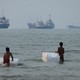 Two children swimming in the Strait of Hormuz with cargo boats in the background
