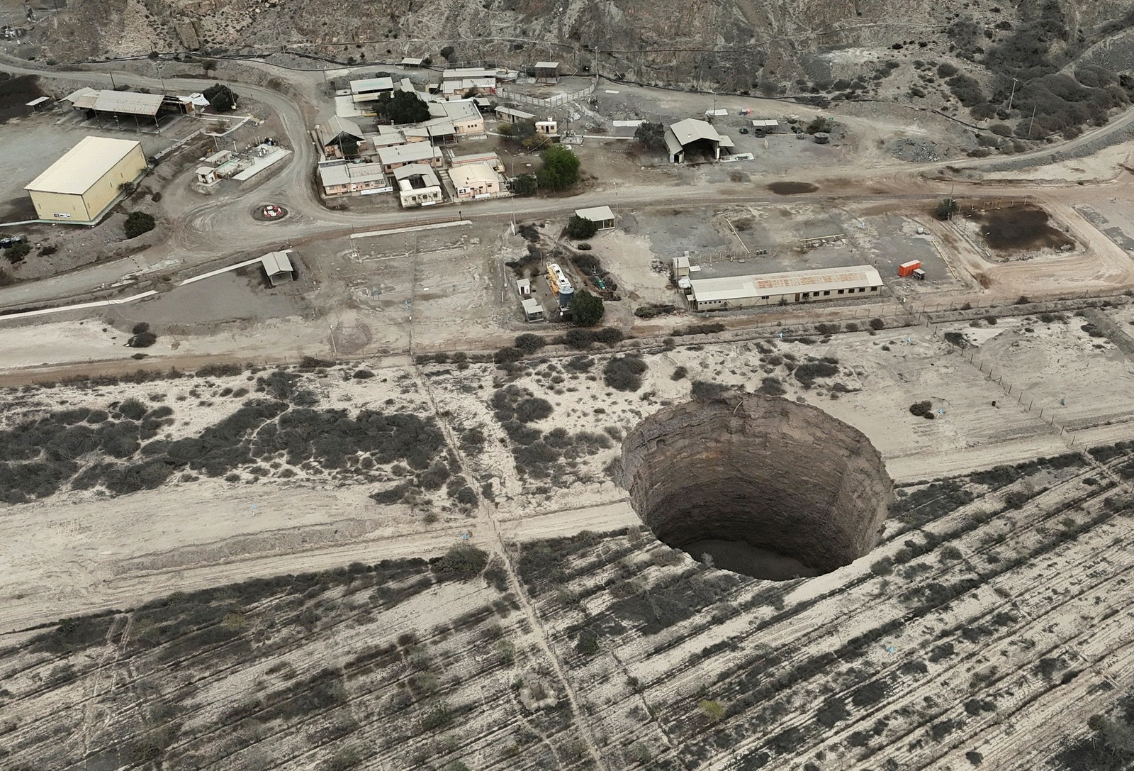 An aerial view of a rural road beside a large circular sinkhole.