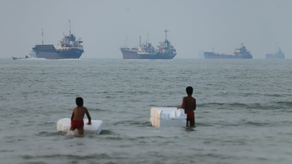 Two children swimming in the Strait of Hormuz with cargo boats in the background