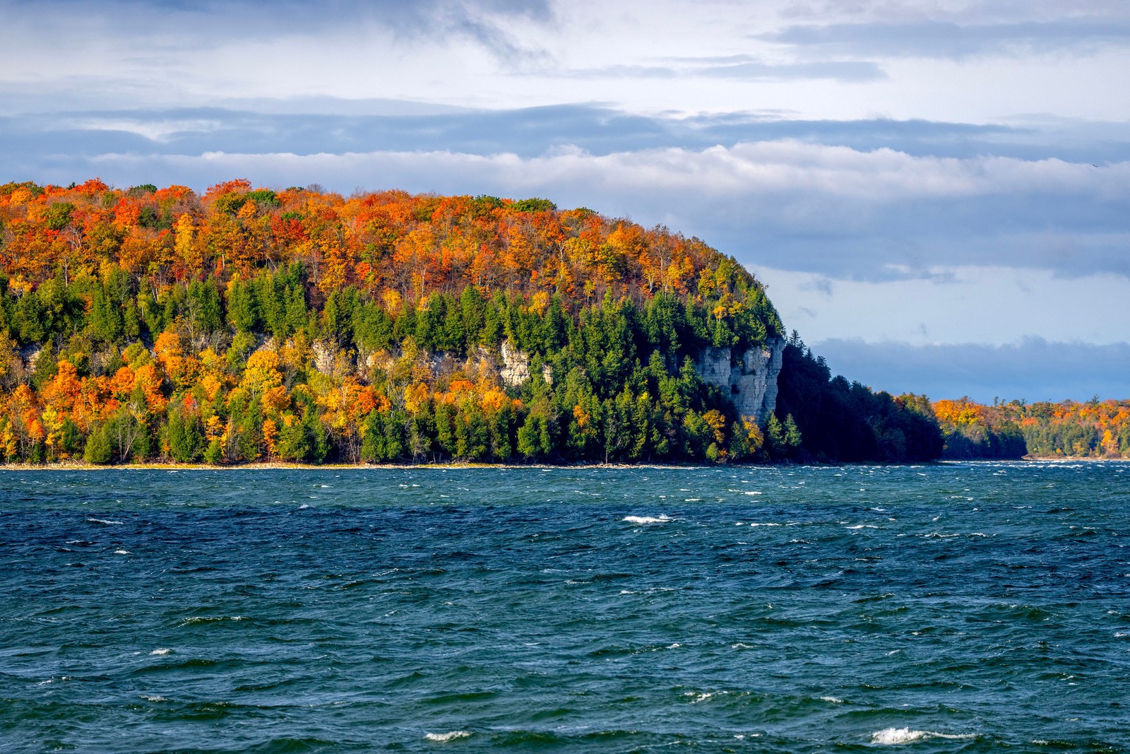 Fall colors cover trees on a bluff above a lake.
