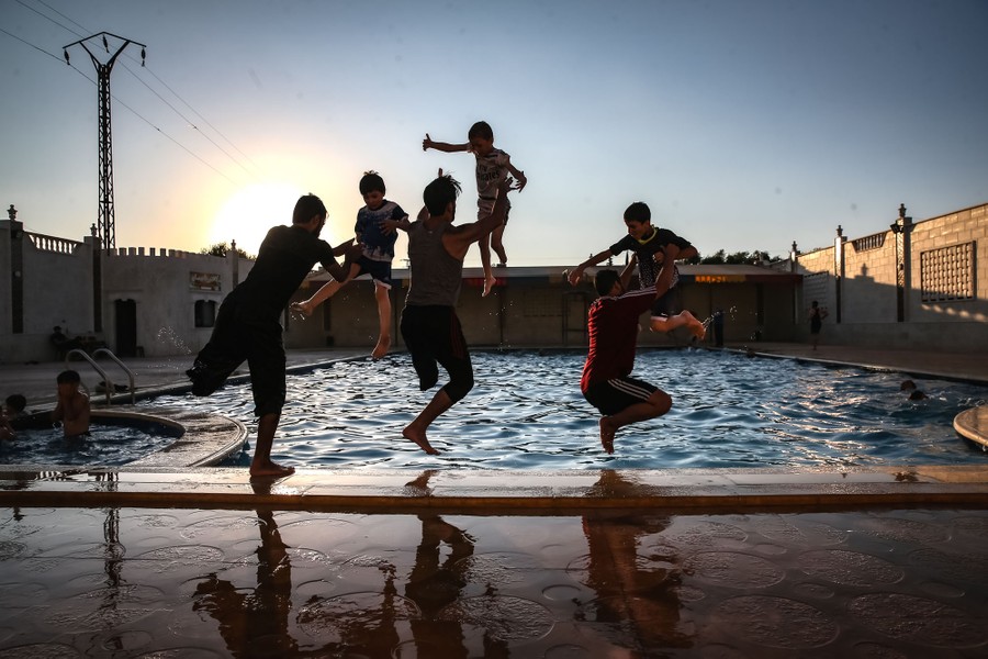 Several young men playfully toss boys into a swimming pool.