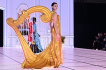 A model walks on a stage wearing a costume shaped like a giant harp.