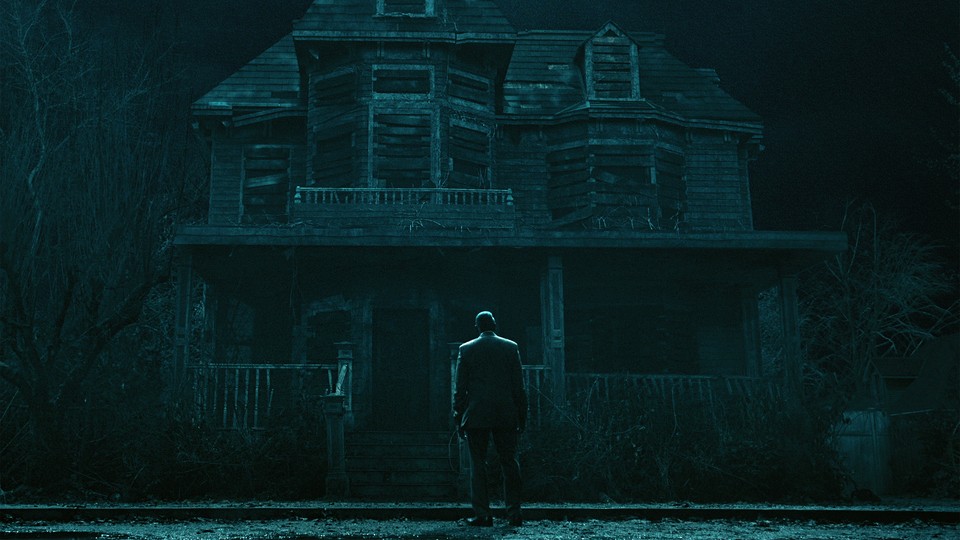man in a suit stands in front of a spooky house at night