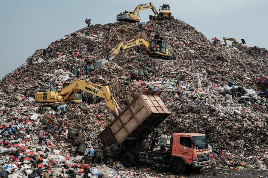 Several excavators, each at different positions on a small mountain of garbage, move newly arrived waste higher up the hill.